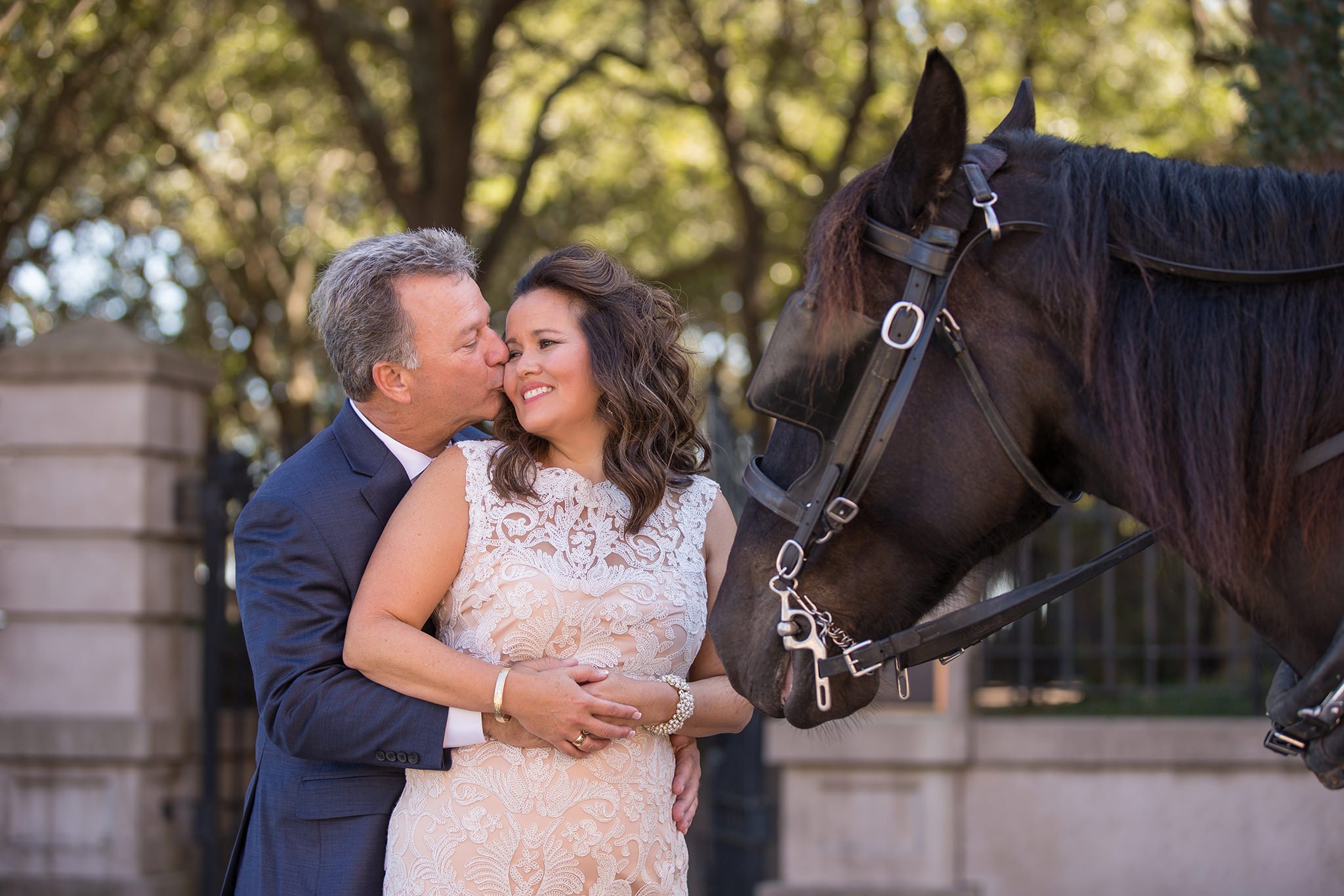 The couple is standing near a horse. The groom is hugging and kissing the bride