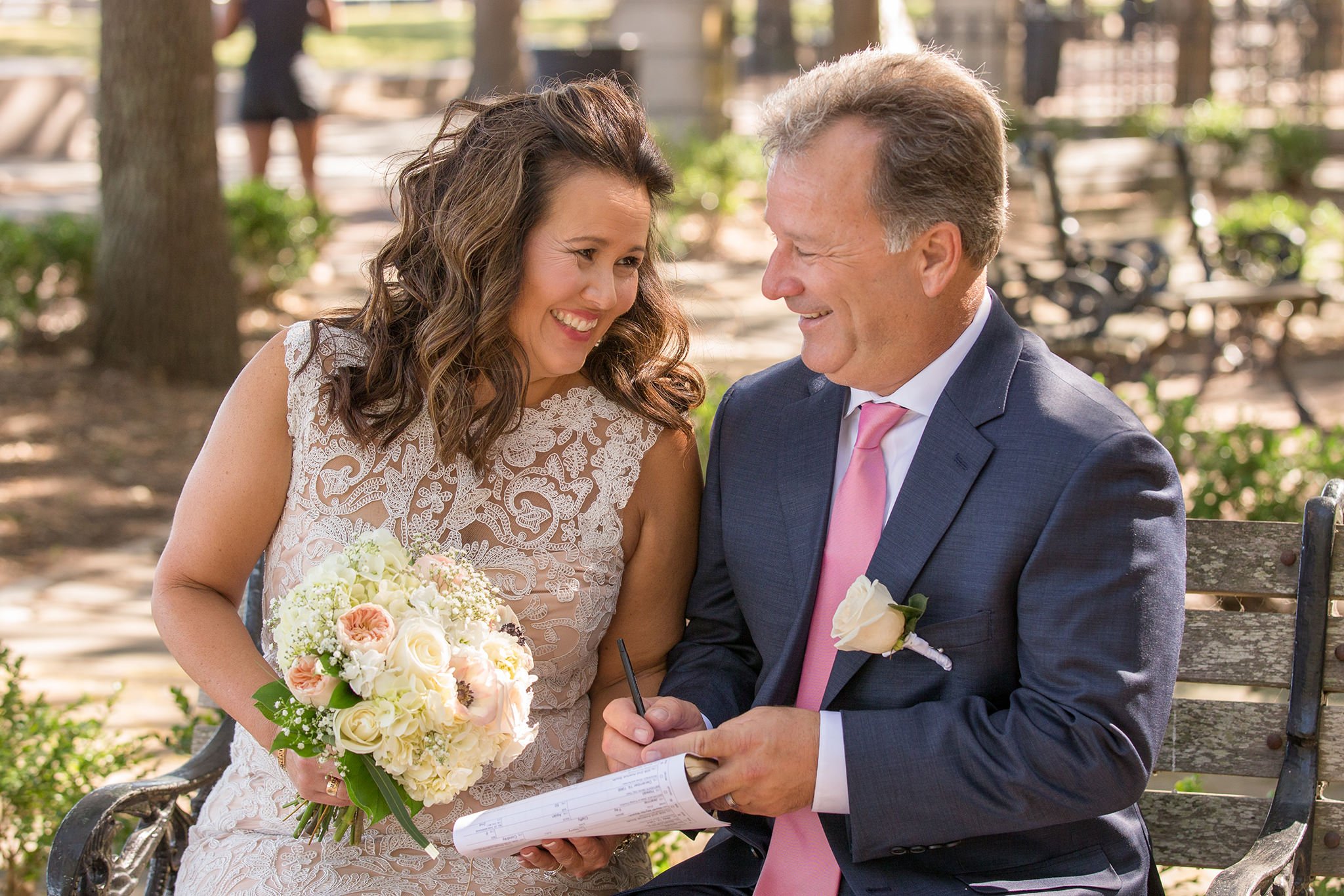 The couple is sitting on the bench, the woman holds the bouquet
