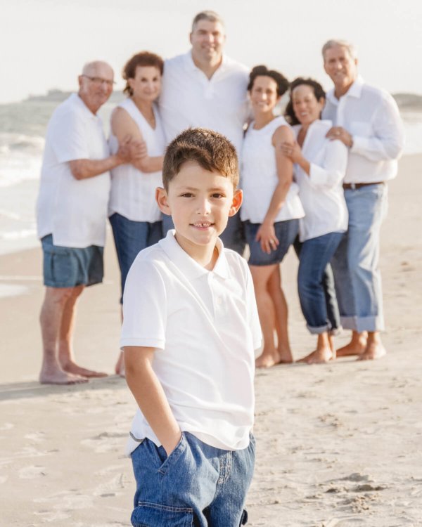 family photo Charleston boy is looking into the camera, the whole family is behind him on the beach