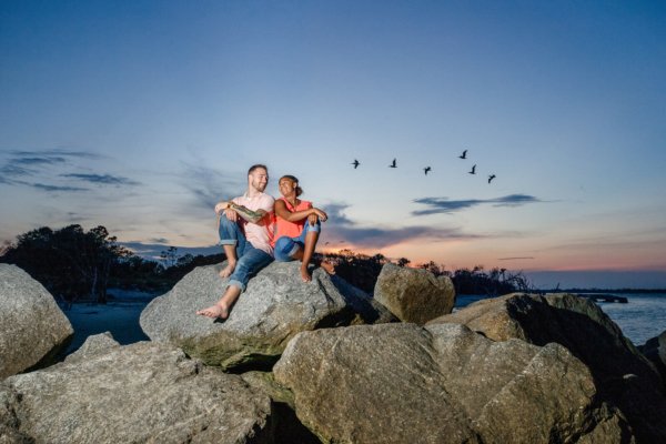 family photo charleston woman and her husband sitting on the rocks during sunset 
