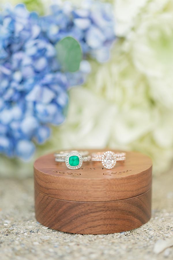 Wedding rings with emerald and diamond set on wooden box with floral background